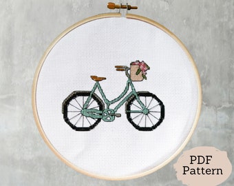 May include: A cross-stitch pattern of a teal bicycle with a basket of flowers on the handlebars. The bicycle has black wheels and brown handlebars. The pattern is on a white background.