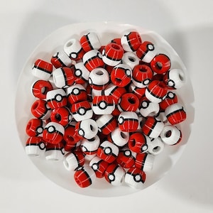 Peut inclure: Une collection de petites perles sph&eacute;riques pr&eacute;sentant un motif rouge et blanc avec une bande horizontale noire et un d&eacute;tail circulaire central noir et blanc, rappelant un design de balle, empil&eacute;es dans un r&eacute;cipient blanc circulaire.