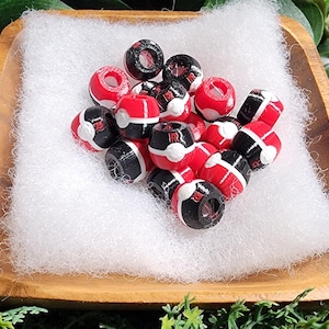 Peut inclure: Une collection de petites perles sph&eacute;riques arborant un motif rouge, blanc et noir. Chaque perle pr&eacute;sente un design &agrave; bandes horizontales distinct avec un cercle blanc central, rappelant un motif de balle classique. Les perles sont lisses.