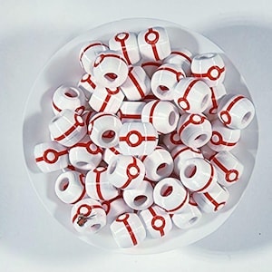 Peut inclure: Une collection de perles blanches en forme de tonneau, orn&eacute;es d'une bande rouge et d'un cercle rouge central, rappelant un r&eacute;cipient sph&eacute;rique. Ces petites perles cylindriques en plastique sont empil&eacute;es, chacune perc&eacute;e en son centre.