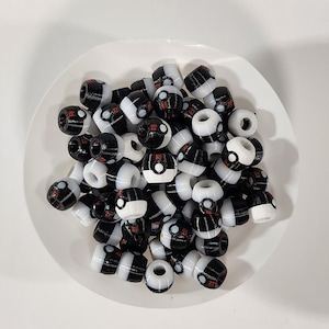 Peut inclure: Une collection de petites perles en plastique en forme de tonneau avec un motif noir et blanc. Chaque perle pr&eacute;sente une ligne horizontale centrale, un petit d&eacute;tail circulaire et une touche rouge, rappelant un contenant sph&eacute;rique.
