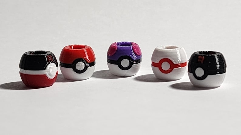 Peut inclure: Cinq perles sph&eacute;riques con&ccedil;ues pour ressembler &agrave; divers r&eacute;cipients en forme de boule. Les perles pr&eacute;sentent des combinaisons de couleurs distinctes, notamment rouge et noir, violet et blanc, et blanc avec des accents rouges, chacune avec un d&eacute;tail circulaire central.