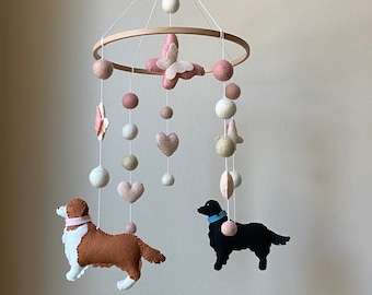 May include: A pink and white felt baby mobile with two felt dogs, hearts, stars, and butterflies hanging from a wooden ring.