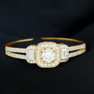May include: A gold ring with a square-shaped centre stone surrounded by smaller diamonds. Two baguette-shaped diamonds are on either side of the centre stone.