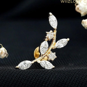 May include: A gold-colored, leaf-shaped earring with marquise-cut and round-cut clear gemstones. The earring has a post backing and is set against a black background. The brand name "WIIZLORI GEMS" is visible in the upper right corner.