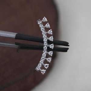 Puede incluir: Un pendiente tipo ear climber de tono plateado con un diseño de barra curva engastado con una hilera de pequeñas piedras redondas transparentes. La pieza incluye nueve piedras individuales en engaste de garra en forma de corona.