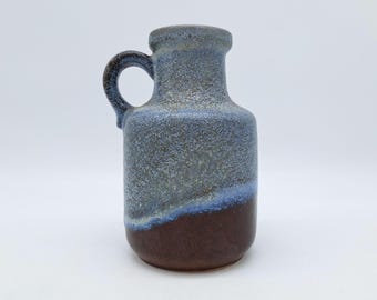 May include: A small, blue and brown ceramic vase with a handle. The vase has a textured glaze and a slightly rounded shape.