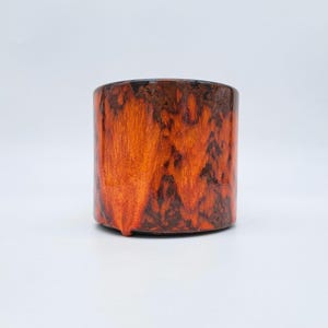 May include: A cylindrical ceramic vase with a glossy finish. The vase has a striking colour gradient, transitioning from dark brown at the top to vibrant orange and reddish-brown hues. The design has a textured, organic appearance.