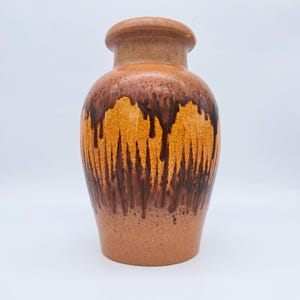 Peut inclure: Un vase en céramique avec un corps arrondi et un col étroit. Le vase présente une base marron terreuse texturée, passant à un motif de glaçure dégoulinante orange vif et marron foncé. Le dessus est de couleur marron uni.