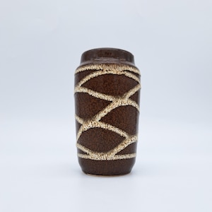 Puede incluir: Un jarrón de cerámica marrón con una superficie texturizada y un patrón entrecruzado en un color beige más claro. El jarrón tiene forma cilíndrica con la parte superior e inferior ligeramente ensanchadas. El diseño es un patrón geométrico.