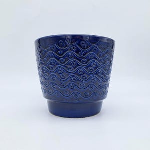 Peut inclure: Un pot de fleurs en céramique bleu foncé avec un motif texturé de vagues et de cercles. Le pot a une forme cylindrique avec un dessus légèrement évasé et une base surélevée. Décoratif, il est adapté à l'intérieur ou à l'extérieur.