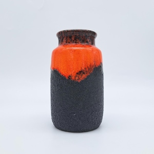 Puede incluir: Un jarrón cilíndrico de cerámica con una base negra texturizada y una sección superior naranja vibrante. El borde es de color marrón oscuro. El jarrón tiene una estética moderna de mediados de siglo y es adecuado para exhibir flores o como acento decorativo.