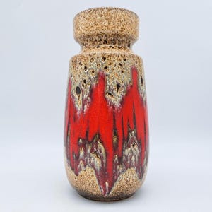 May include: A ceramic vase with a textured, speckled finish. The top and base are a light brown, while the body features a vibrant red glaze with streaks of white and brown. The vase has a cylindrical shape with a slightly flared top.