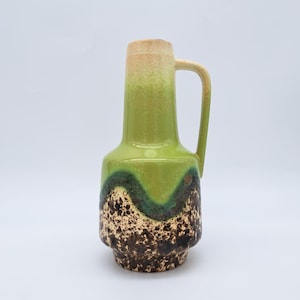 May include: A vintage ceramic vase with a handle, featuring a green and brown speckled design. The vase has a tall, slender neck that transitions from light tan to green. The body has a textured, speckled pattern.