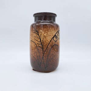 Puede incluir: Un jarrón de cerámica marrón con una superficie texturizada y un borde marrón oscuro. El jarrón presenta un diseño floral estilizado en marrón oscuro. El jarrón mide unos 20 cm de alto.