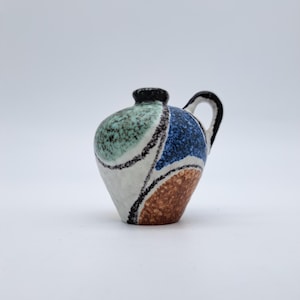 May include: A small, decorative ceramic pitcher with a black handle and rim. The body is adorned with a colorful abstract design featuring blue, brown, green, and white sections separated by black lines. The pitcher has a rounded body and a small spout.
