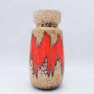 May include: A vintage ceramic vase with a cylindrical shape. The vase features a speckled beige top and base, with a vibrant red glaze cascading down the center. The red glaze has a textured, dripped appearance, creating a unique aesthetic.