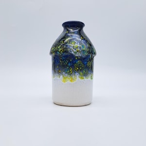 Puede incluir: Una taza de cerámica blanca con un asa negra y el texto "But First, Coffee" en negrita negra. La taza se encuentra sobre un fondo borroso, sugiriendo un ambiente acogedor.