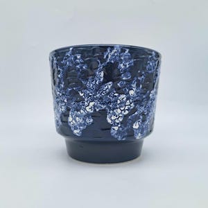 Peut inclure: Un pot de fleurs cylindrique en céramique présentant une base bleu marine profond avec un motif en relief texturé. La partie supérieure est ornée d'un effet d'émail blanc tacheté, semblable à une éponge, contrastant avec le fond bleu.