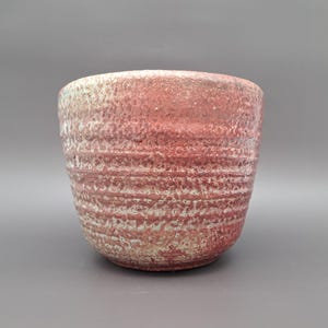 Könnte beinhalten: Eine kleine, rote und weiße Keramikschale mit strukturierter Oberfläche. Die Schale hat eine abgerundete Form und einen leicht ausgestellten Rand.