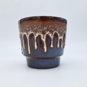 May include: A ceramic mug featuring a dark brown and blue glaze with a distinctive white drip pattern cascading from the rim. The vessel has a wide, rounded top that tapers down to a narrower base, showcasing a smooth, glossy finish throughout.