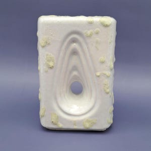 May include: White ceramic vase with a textured surface and a hole in the center. The vase has a unique, abstract design.