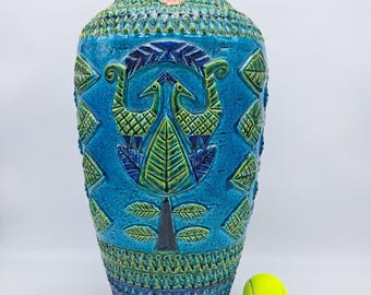 May include: A large, blue and green ceramic vase with a raised design of birds and leaves. The vase has a textured surface and is decorated with a geometric pattern.