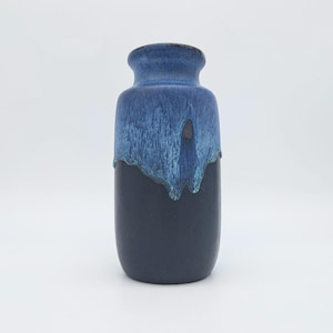 Op de afbeelding: Een tweekleurige blauwe keramische vaas. De bovenste helft heeft een lichtere, getextureerde blauwe glazuur die over de donkerdere blauwe basis druipt. De vaas heeft een afgeronde body en een smalle hals.