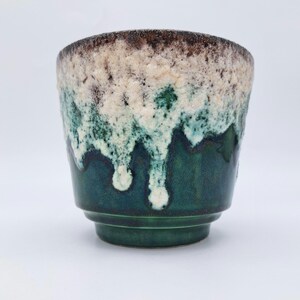 Puede incluir: Una taza de cerámica con una base de color verde oscuro que transiciona hacia un esmalte texturizado de color blanco roto cerca del borde. La parte superior muestra un acabado moteado en marrón y crema con un patrón de goteo definido.
