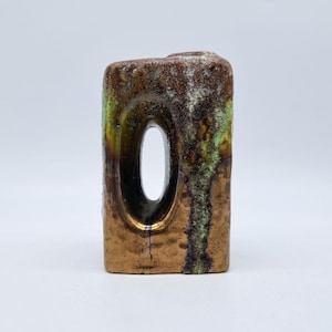 Puede incluir: Un jarrón rectangular de cerámica con una gran abertura ovalada. El jarrón tiene una base de bronce con detalles en marrón, verde y blanco. El jarrón mide aproximadamente 13 cm de alto.