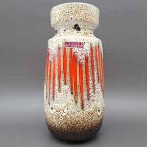 May include: A tall, white ceramic vase with a brown and orange glaze. The vase has a wide mouth and a narrow base. It has a label that says "scheurich".