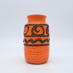 Puede incluir: Jarrón de cerámica naranja con diseños negros en espiral y líneas onduladas. El jarrón tiene una superficie texturizada y una forma cilíndrica, con una parte superior ligeramente ensanchada. El diseño es de estilo retro, adecuado para la decoración del hogar.