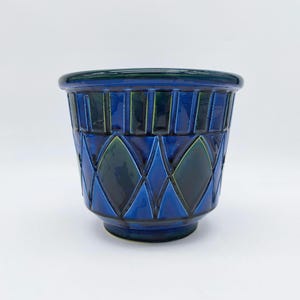 Puede incluir: Un macetero de cerámica azul y verde con un patrón geométrico de diamantes. El macetero tiene una base ancha y una abertura estrecha.
