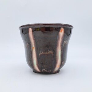 Op de afbeelding: Een keramische plantenpot met een glanzend donkerbruin glazuur. De buitenkant is voorzien van verticale, langwerpige strepen in lichtbeige en subtiele oranje tinten die een druipend effect creëren op de diepe, donkerbruine basis van de kom.