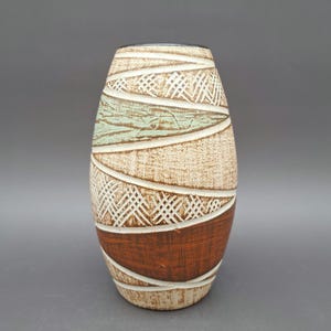 Puede incluir: Un jarrón de cerámica con un patrón geométrico marrón, blanco y verde. El jarrón tiene una forma redondeada y ovalada.