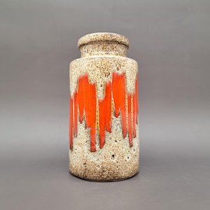 Peut inclure: Un vase cylindrique en céramique avec une glaçure texturée et mouchetée beige et brune. La partie supérieure est ornée d'un motif de coulures orange vif et brillant qui descend sur la surface neutre à l'aspect poreux.