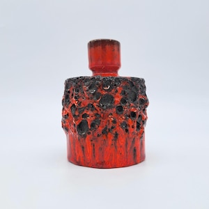 Peut inclure: Un bougeoir en céramique rouge et noir avec un design texturé en forme de lave. La base cylindrique se transforme en un sommet cylindrique plus petit. La palette de couleurs est principalement rouge avec des accents noirs.