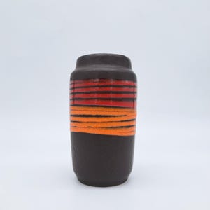 Puede incluir: Un jarrón cilíndrico de cerámica con base y parte superior marrón oscuro. La sección media presenta bandas horizontales rojas y naranjas. El jarrón tiene una superficie texturizada y un diseño simple y clásico. Es adecuado para exhibir flores o como objeto decorativo.
