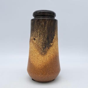 Könnte beinhalten: Eine braune und beige Keramikvase mit strukturierter Oberfläche. Die Vase hat eine zylindrische Form mit leicht ausgestelltem Boden und einem dunkelbraunen Rand. Die Farben gehen von Dunkelbraun zu Beige über.