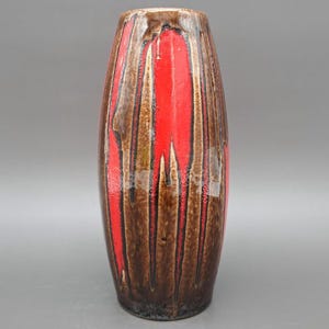 Peut inclure: Un vase en céramique brun et rouge avec un motif rayé. Le vase est haut et fin, avec un fond arrondi et un sommet légèrement évasé.