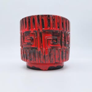 May include: A cylindrical red and black ceramic planter with a geometric design. The planter features vertical ridges and square patterns, with a glossy finish. The base is a darker shade of red.