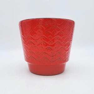 May include: A vibrant red ceramic planter with a textured, wave-like pattern. The planter has a slightly flared top and a sturdy base. This decorative piece is suitable for small plants or as a stylish accent.
