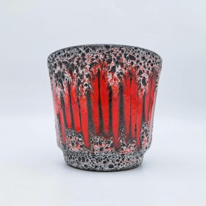 Puede incluir: Una maceta de cerámica con un diseño llamativo. El exterior presenta una base roja vibrante con vetas negras verticales, contrastada por un borde texturizado en blanco y negro. La maceta tiene forma cilíndrica y es adecuada para plantas de interior.