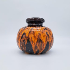 Peut inclure: Un vase en céramique avec un corps arrondi et un bord marron foncé. Le vase présente un motif saisissant de glaçure orange et noire, créant un design texturé en forme de flamme. C'est un objet décoratif.