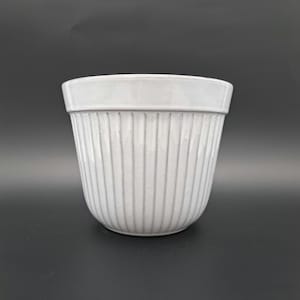 Op de afbeelding: Witte keramische plantenpot met verticale ribbels. De pot heeft een ronde bodem en een brede, licht uitlopende opening.