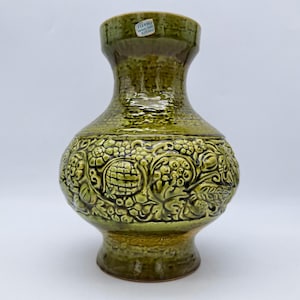 Könnte beinhalten: Eine grüne Keramikvase mit strukturierter Oberfläche und geprägtem Blumendesign. Die Vase hat einen breiten Boden und einen schmalen Hals. Das Etikett auf der Vase lautet "Handgefertigt in Italien".