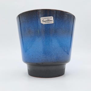 Peut inclure: Un cache-pot en céramique à la silhouette effilée, doté d'une finition dégradée brillante passant d'une base noire profonde à une section supérieure bleu roi éclatante. Une étiquette blanche rectangulaire indique Tönnieshof Carstens W-Germany.