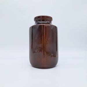 May include: A brown ceramic bottle with a glossy finish. The bottle has a cylindrical body with a slightly rounded base and a narrow neck. The color is a rich, dark brown.