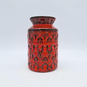 May include: A red and black ceramic vase with a geometric pattern. The vase is about 6 inches tall and has a narrow opening.