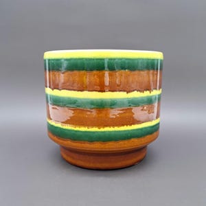 Op de afbeelding: Een bruine keramische plantenpot met groene en gele strepen. De pot heeft een afgeronde basis en een brede opening.